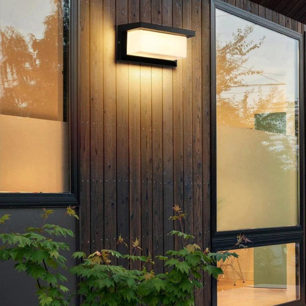 Wall light mounted on dark vertical wood siding between large windows, with maple foliage in the foreground. 5