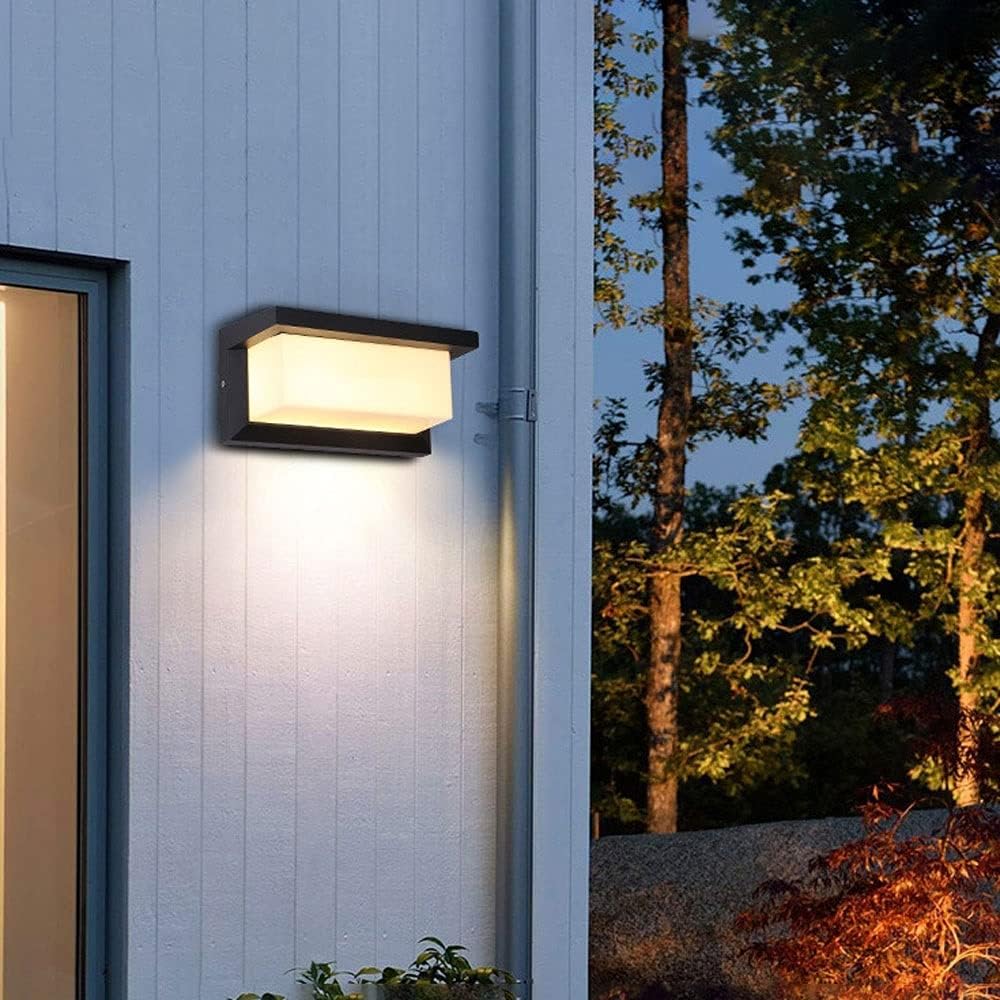 Wall light glowing on a white clapboard house wall next to a window and downspout, with trees behind. 6