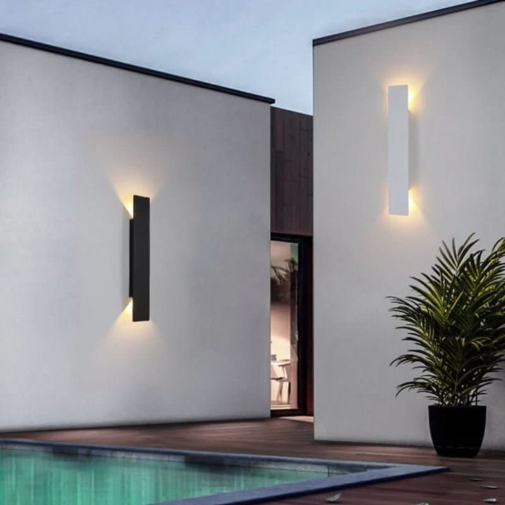 Black and white vertical wall lights mounted on separate white walls beside a pool at dusk, each glowing warmly up and down. 4