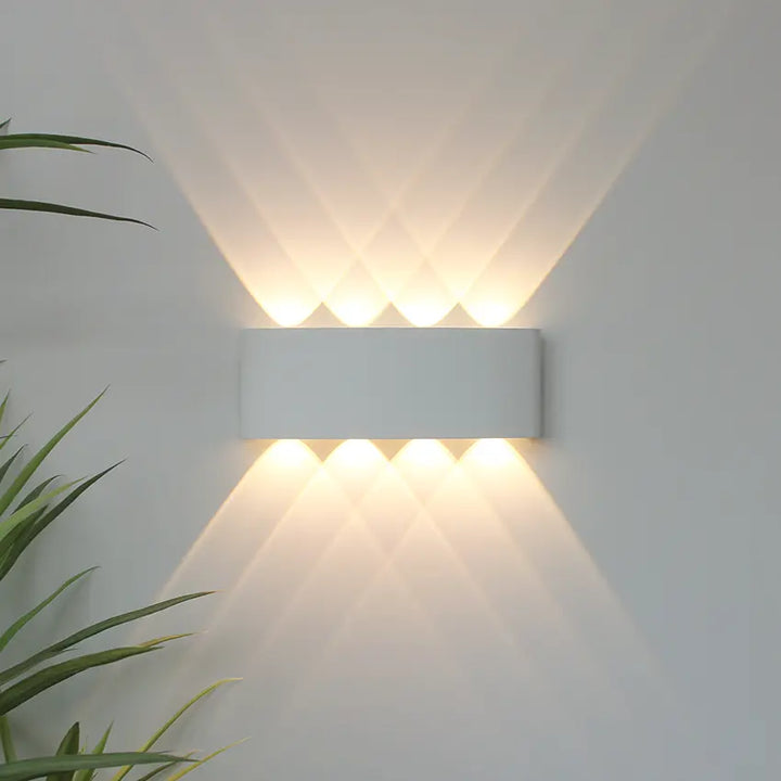 White Skøle wall light fixture with curved shape mounted on a gray wall casting warm light upward and downward