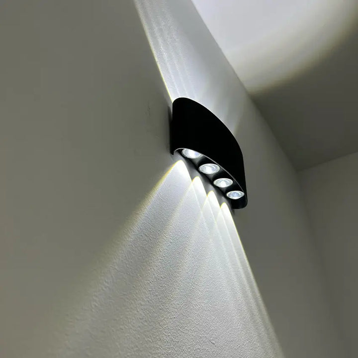 Black Skøle wall light fixture detail with four lens openings casting bright beams along a corner wall