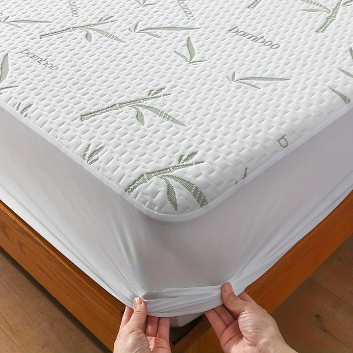 Close-up of a mattress corner wrapped in the white quilted cover with a green bamboo leaf pattern, hands pulling the stretchy skirt. 1