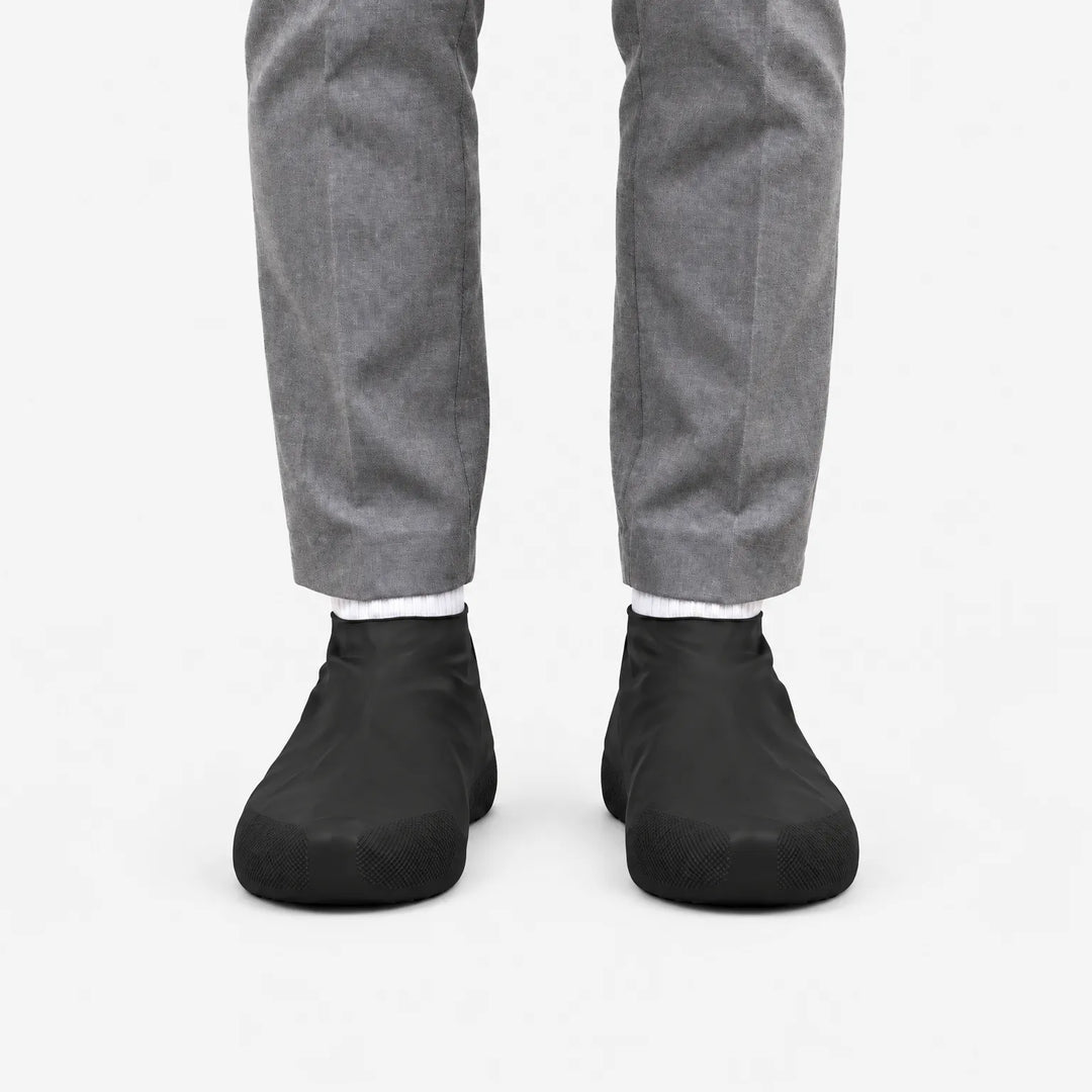 Front view of black shoe covers worn with gray trousers and white socks on a plain white background. 4