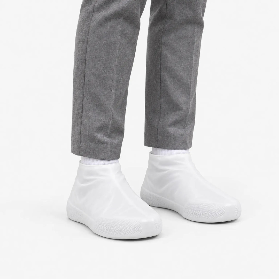 Angled view of translucent white shoe covers worn with gray trousers, showing the textured sole at the toe. 5