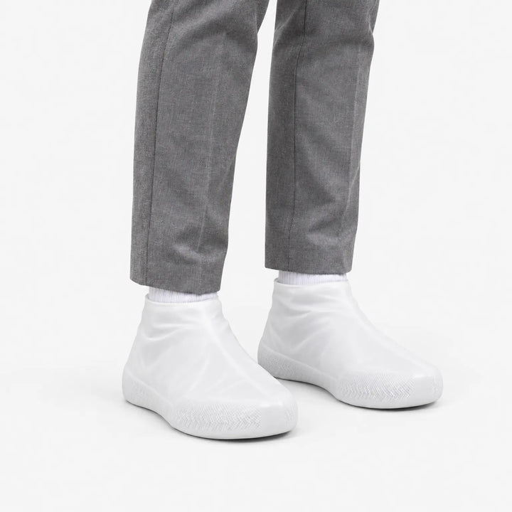Angled view of translucent white shoe covers worn with gray trousers, showing the textured sole at the toe. 5