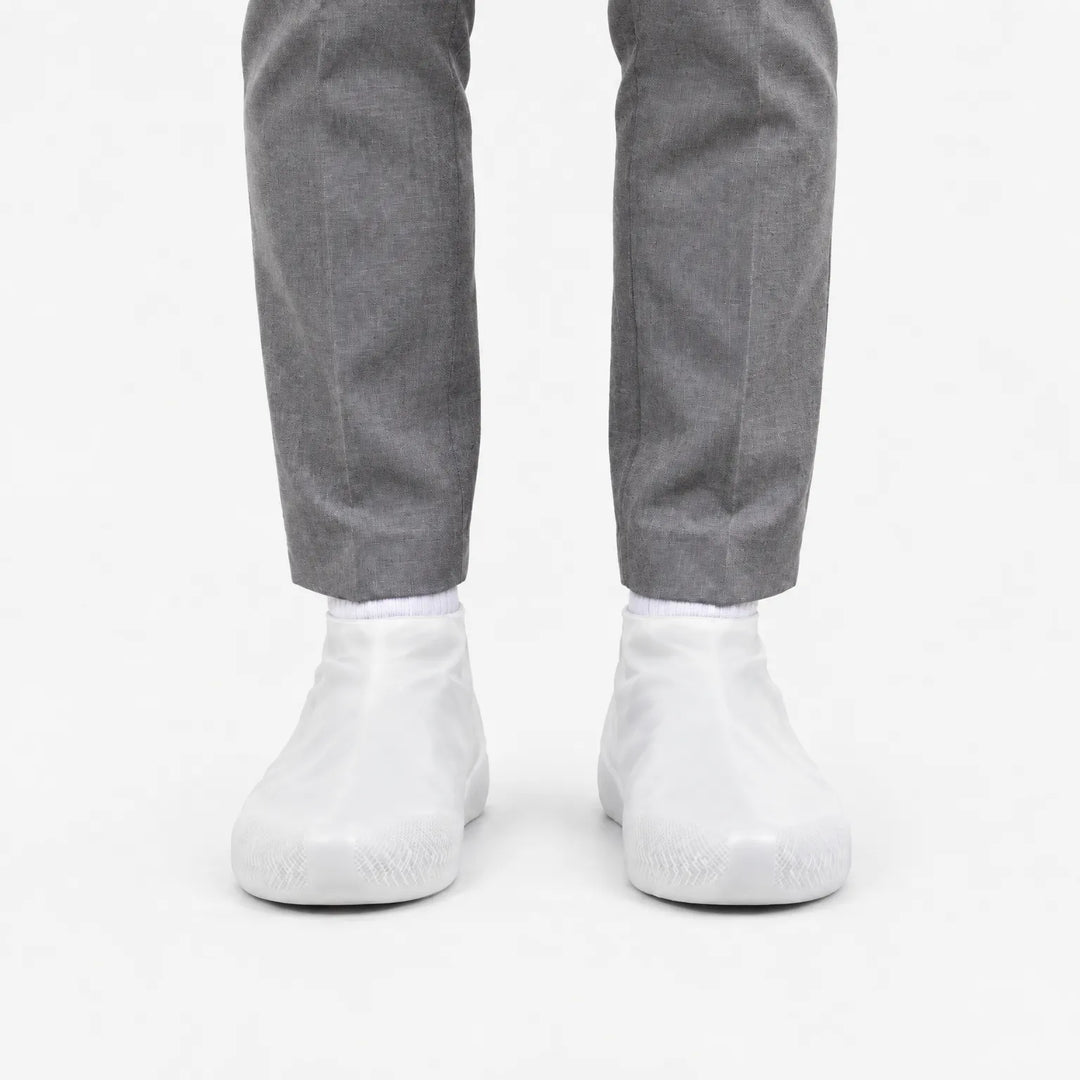 Front view of translucent white shoe covers worn with gray trousers and white socks, showing the grip pattern at the toes. 8