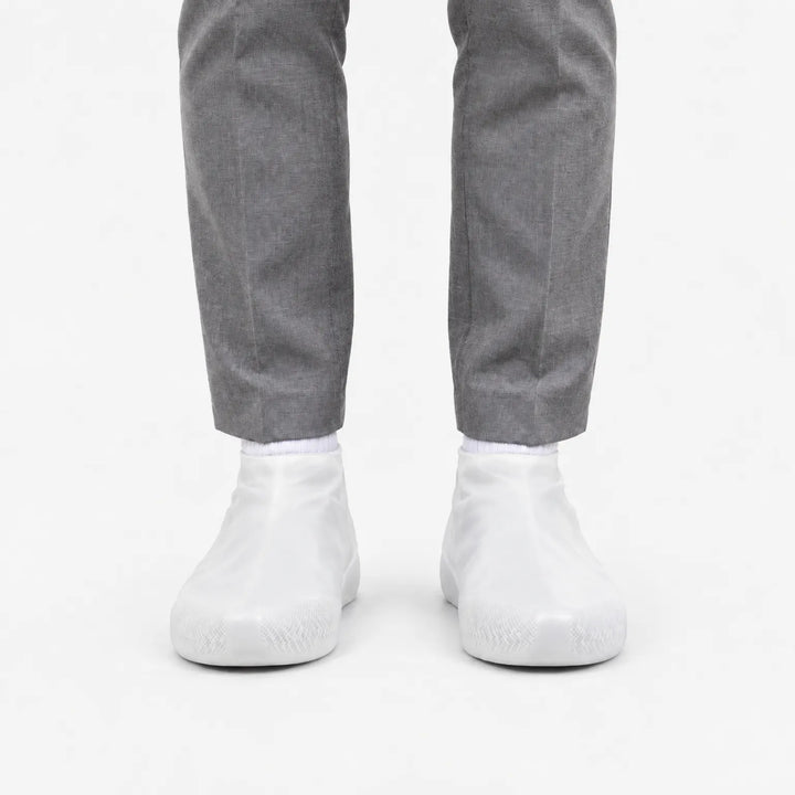 Front view of translucent white shoe covers worn with gray trousers and white socks, showing the grip pattern at the toes. 8