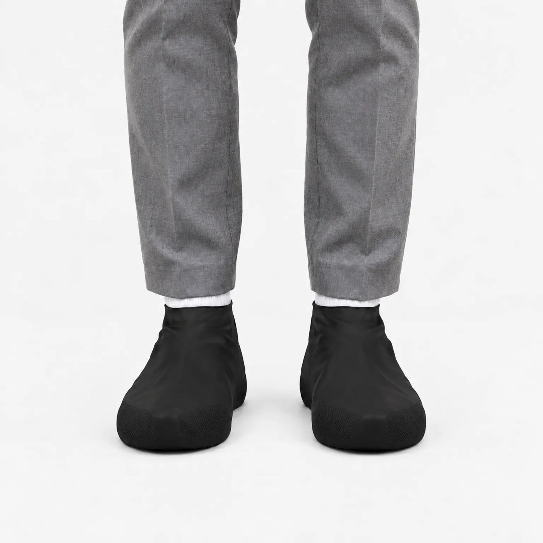 Second front view of black shoe covers worn with gray trousers and white socks on a white background. 9