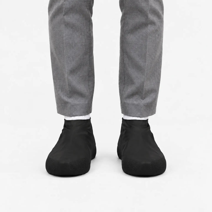 Second front view of black shoe covers worn with gray trousers and white socks on a white background. 9
