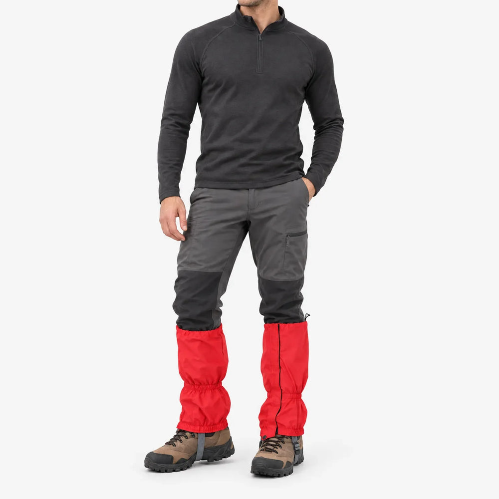 Full-length studio view of a man in a dark pullover and gray hiking pants wearing red gaiters over hiking boots. 2