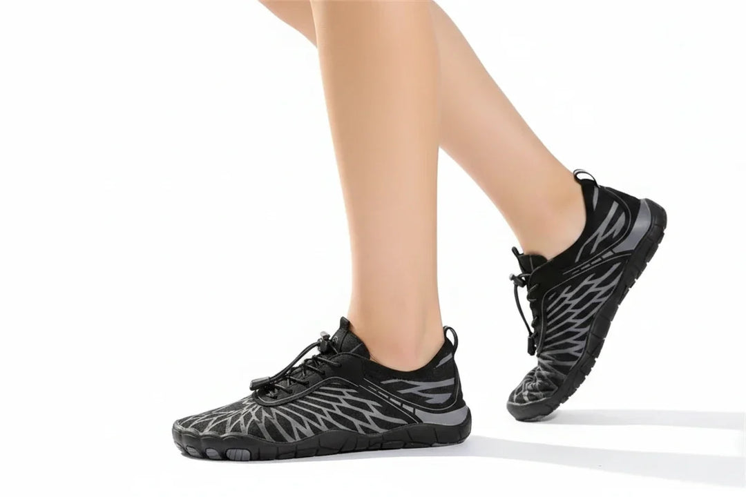 Side view of a woman walking in black barefoot shoes with gray patterned overlays and bungee laces on a white background.