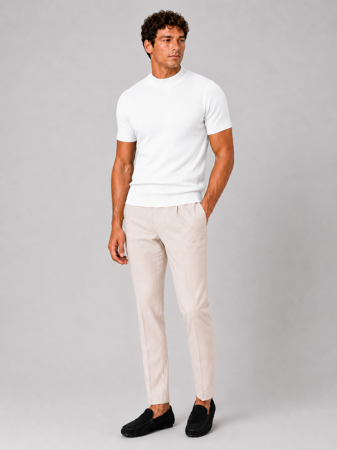 Men's white ribbed tee worn with cream pleated trousers and black suede loafers, front view.
