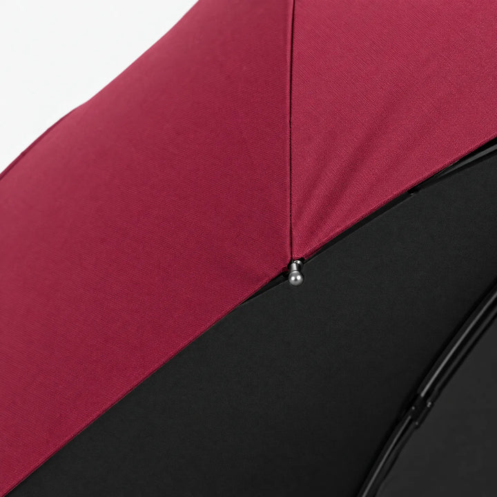 Close-up detail of a burgundy canopy seam and a small metal rib tip above the black underside lining. 4
