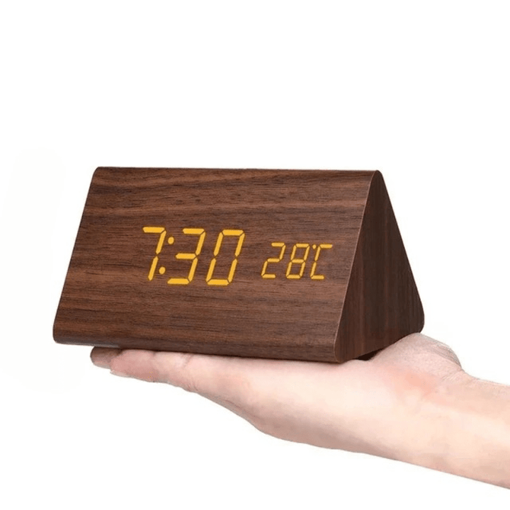 Dark brown wood-grain triangular LED clock with amber digits held in a palm.