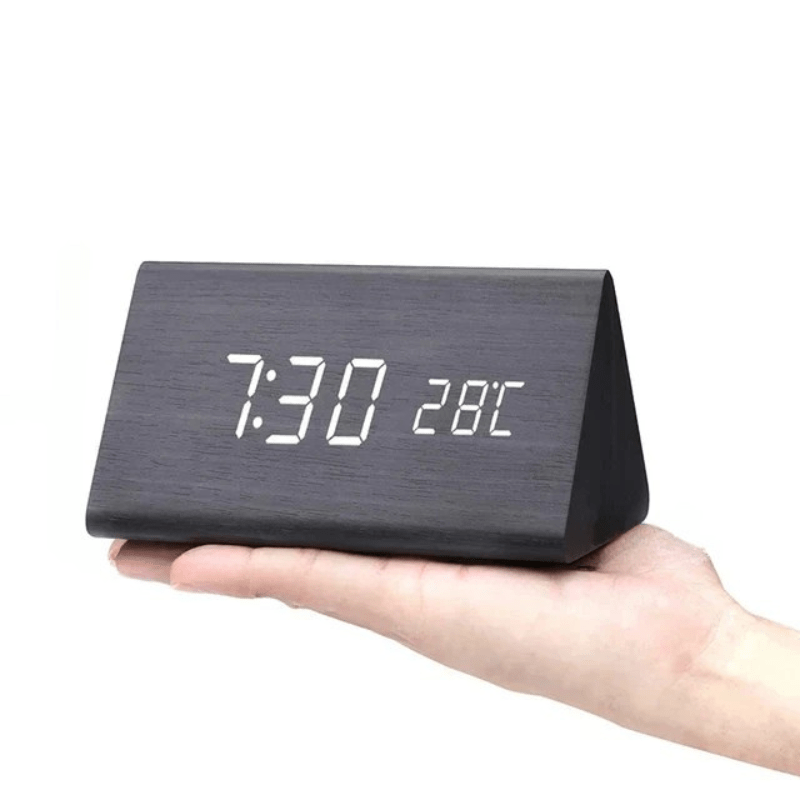 Black wood-grain triangular clock with white LED digits balanced on an open palm.