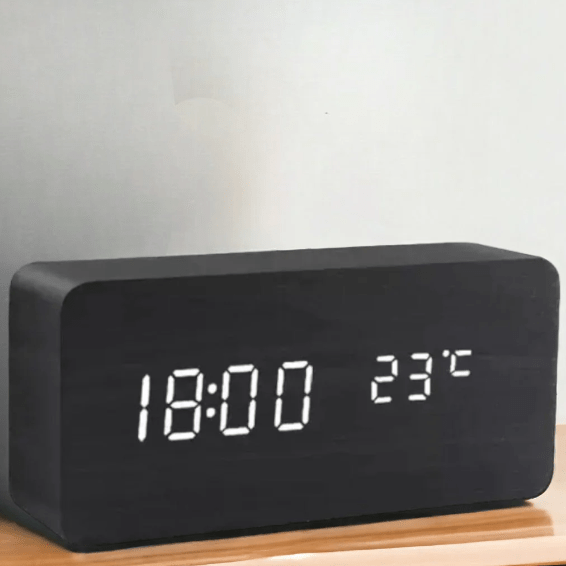 Black rectangular clock with white LED digits on a wooden surface.