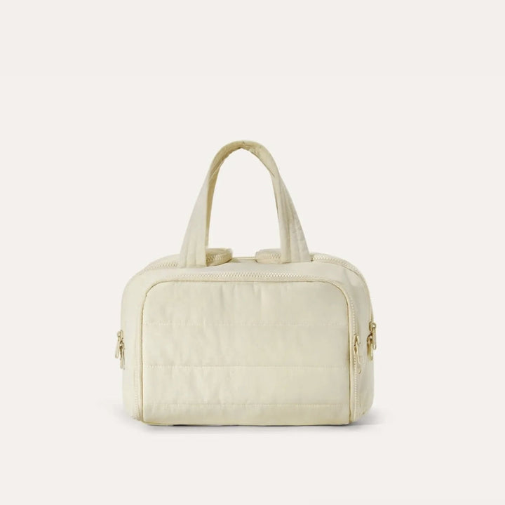 Quilted toiletry bag in cream, front view, with two top handles and zipper pulls on both sides. 16