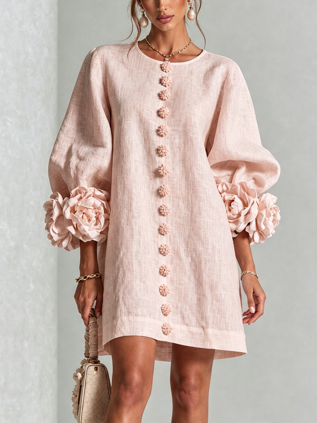 Light blush pink shirt dress on a model, front view, with flower-shaped buttons down the center and large rose cuffs. 24