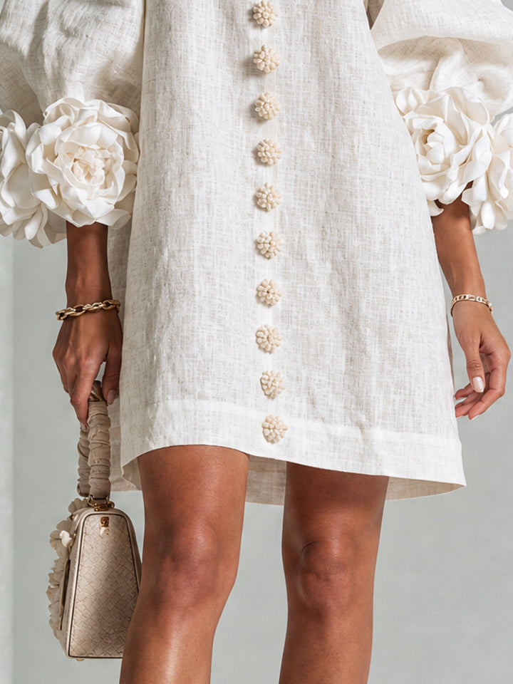 Beige dress detail showing the floral button row, hem and rosette cuffs.