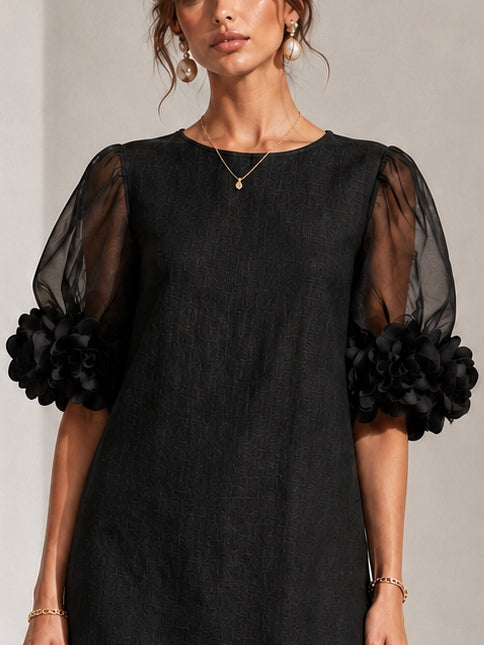 Detail of the round neckline and sheer puff sleeves with floral appliqué detail on the black dress