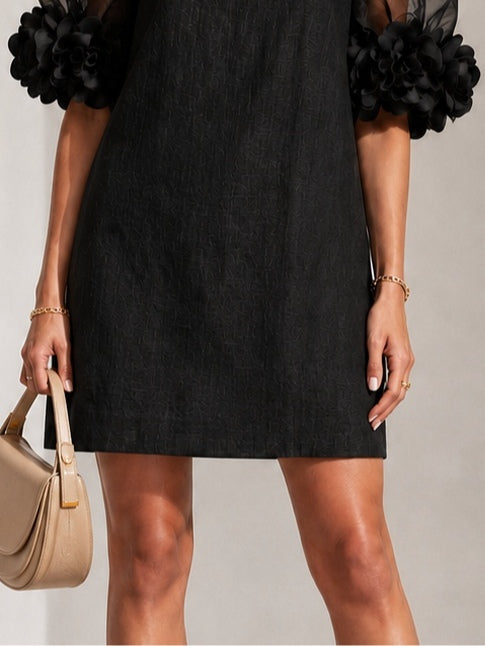 Detail of the lower half of the black dress with textured fabric and straight hem