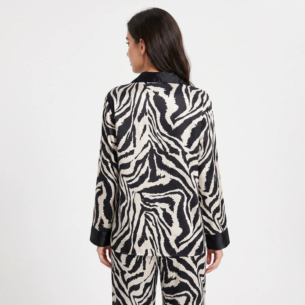 Back view of a model in the long-sleeve zebra-print satin pajama top with black collar and cuffs, paired with matching pants. 2