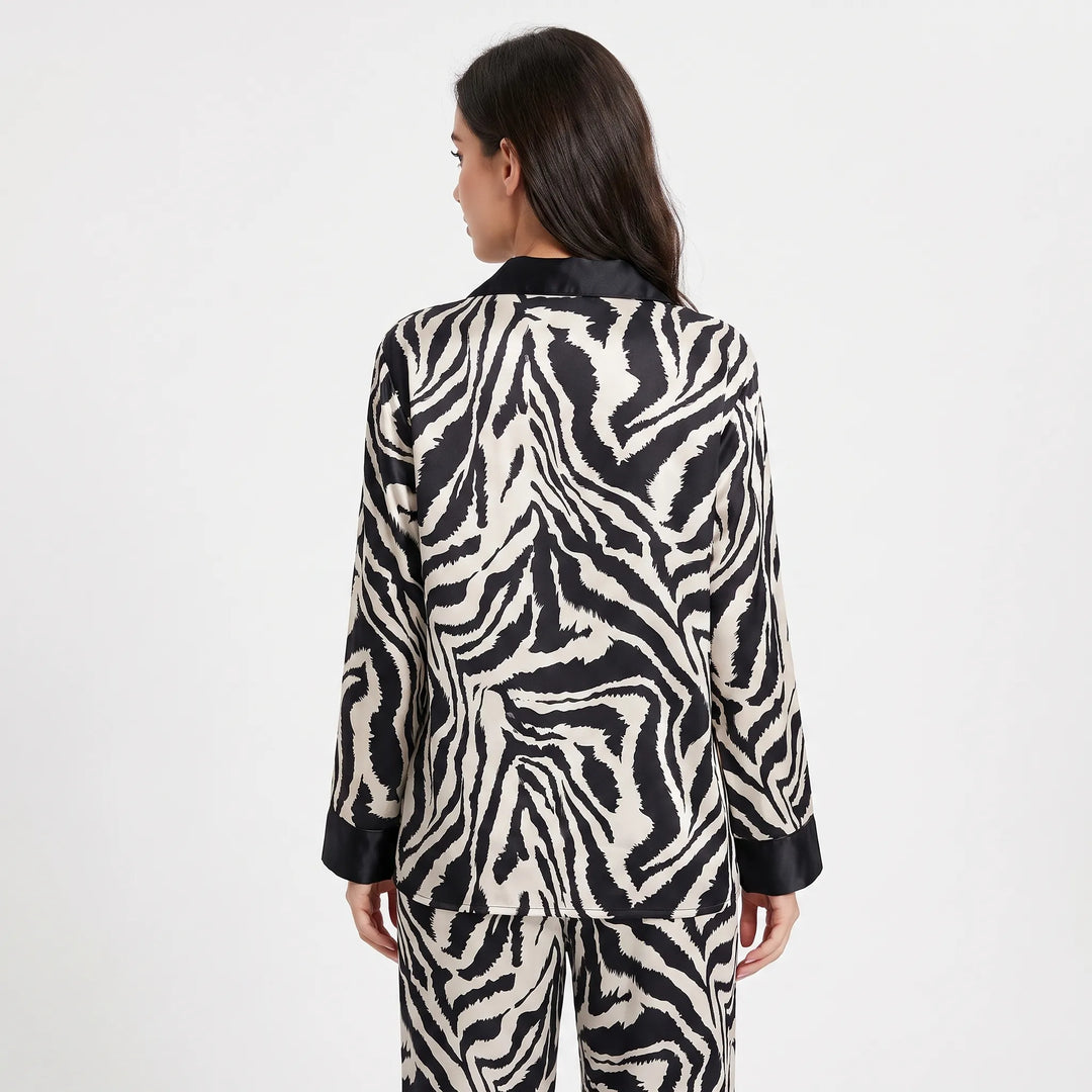Back view of a model in the long-sleeve zebra-print satin pajama top with black collar and cuffs, paired with matching pants. 2
