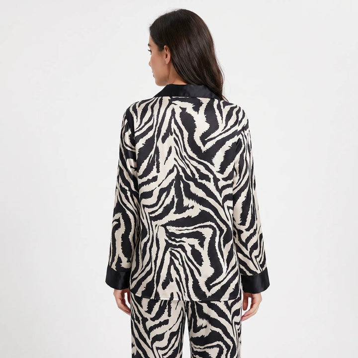 Back view of a model in the long-sleeve zebra-print satin pajama top with black collar and cuffs, paired with matching pants. 2
