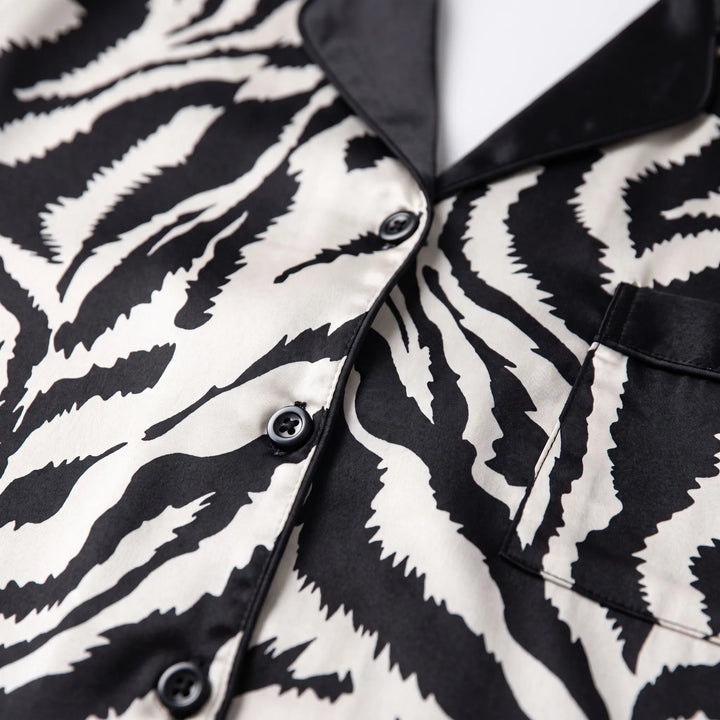 Close-up of the black notched collar, black buttons and trimmed chest pocket on the zebra-print satin pajama top. 4