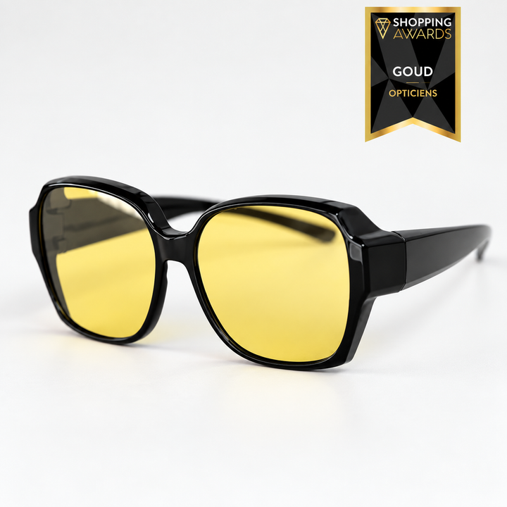 Three-quarter front view of oversized glossy black frame glasses with yellow-tinted lenses.
