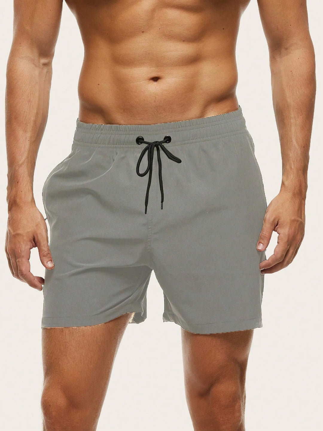 Men's swim trunks in light gray on a model, front view with a black drawstring and elastic waistband.
