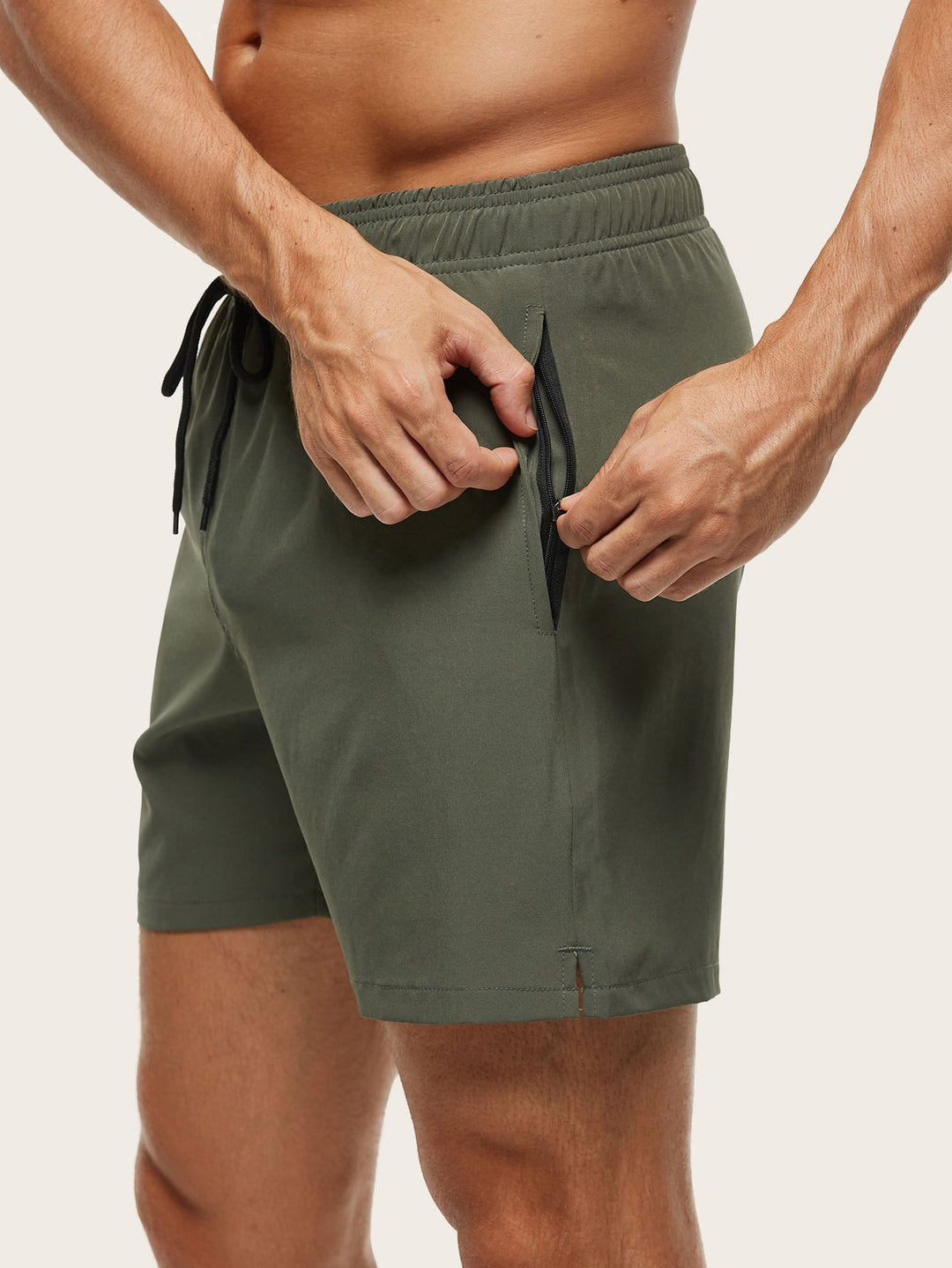 Men's swim trunks in olive green, detail of hands opening the black zippered side pocket and a small hem slit.