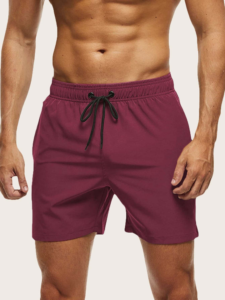 Men's swim trunks in burgundy on a model, front view with black drawstring tied at the elastic waist.
