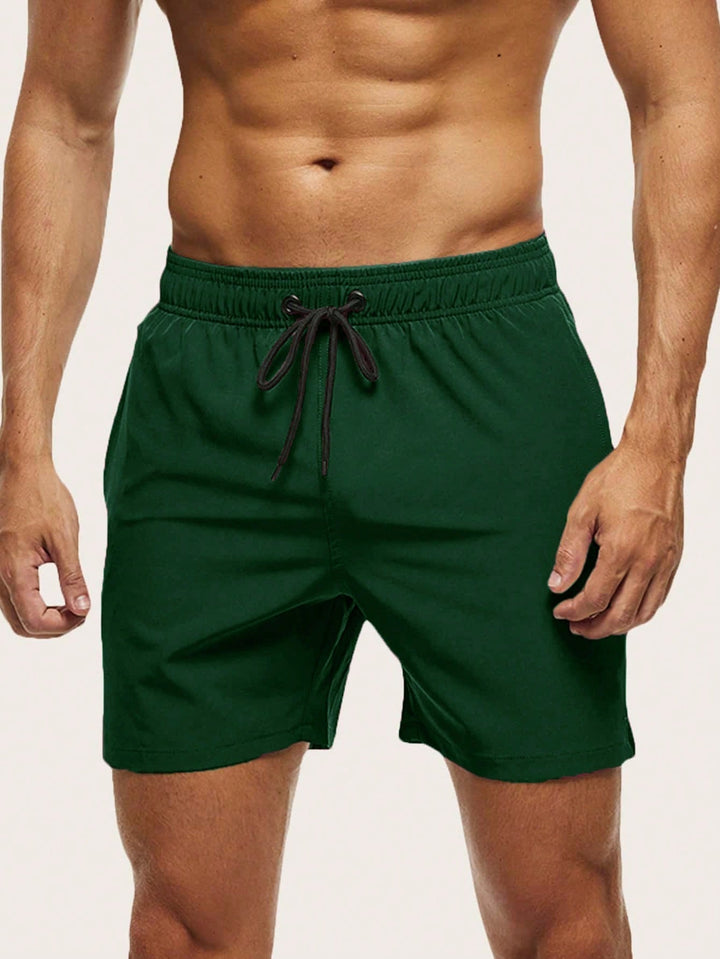 Men's swim trunks in dark green on a model, front view with black drawstring and short straight legs.