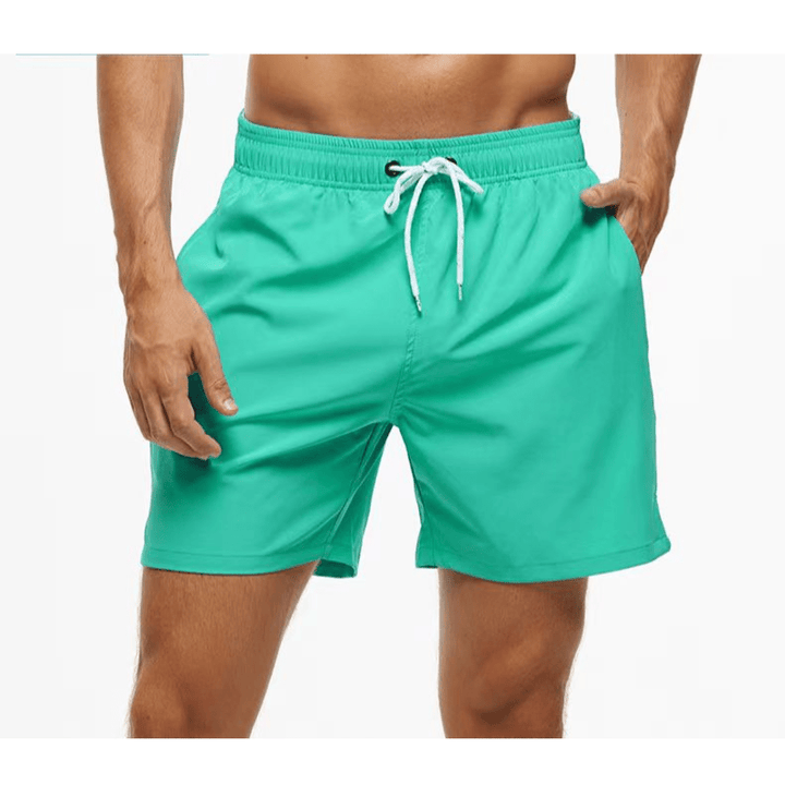 Mint green swim trunks with a white drawstring and elastic waistband, worn with one hand in a side pocket. 8