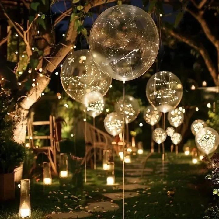 Clear light-up balloons among trees and lanterns along a nighttime garden path