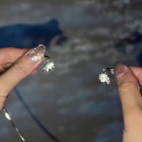 Two hands with sparkly nails each hold one half of the necklace's split heart clasp, showing the pieces separated before they connect. 1