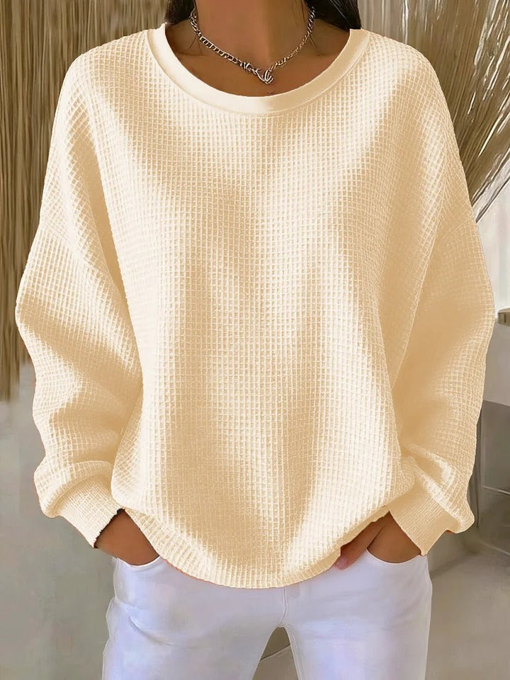 Pale cream waffle-texture pullover with hands tucked into white pants pockets.