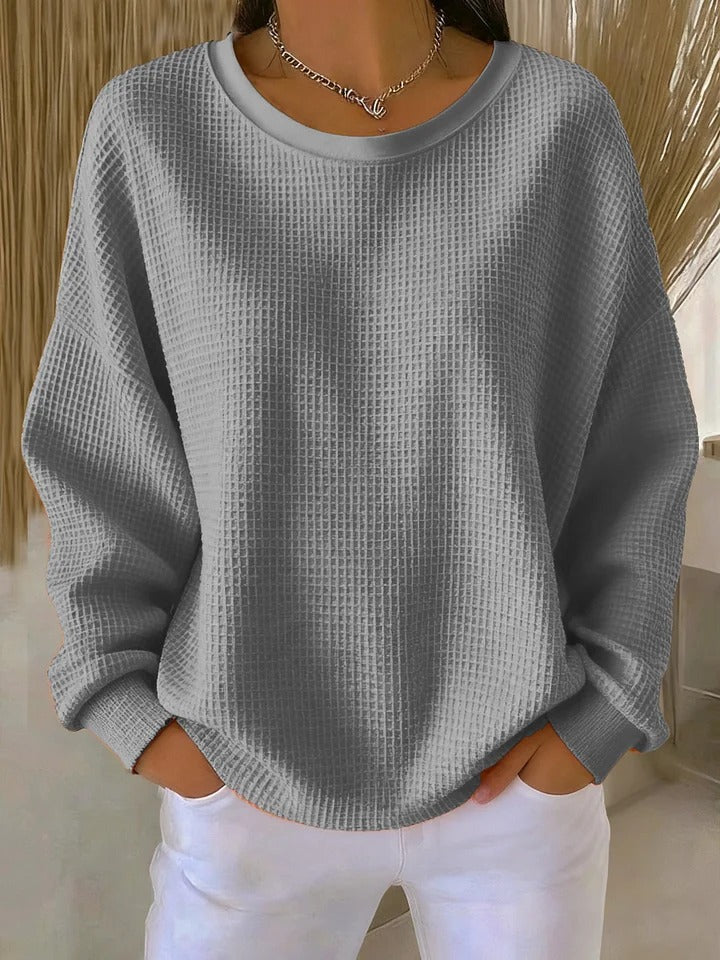 Grey textured crew neck sweater with relaxed drop-shoulder sleeves and a chain necklace.