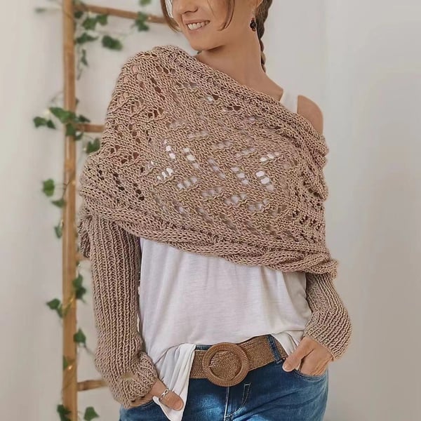 Tan taupe wrap draped off one shoulder with open lace stitching and ribbed sleeves, paired with a woven belt and jeans. 20