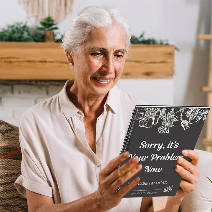 Smiling older woman with white hair holds up the dark floral planner cover in a living room 5