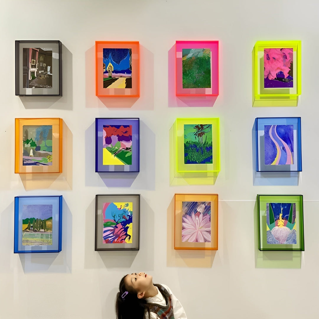 Wall display of twelve wall-mounted acrylic frames in neon orange, pink, yellow, blue and green, each holding a colorful painting, with a child looking up. 22