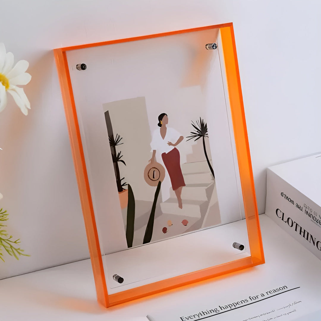 Orange-edged acrylic frame leaning on a white shelf beside white flowers.