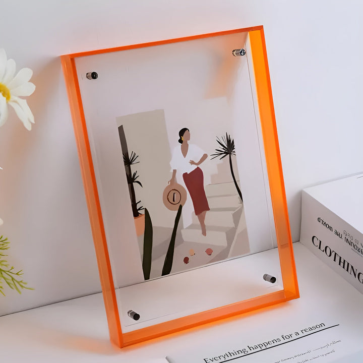 Orange-edged acrylic frame leaning on a white shelf beside white flowers.