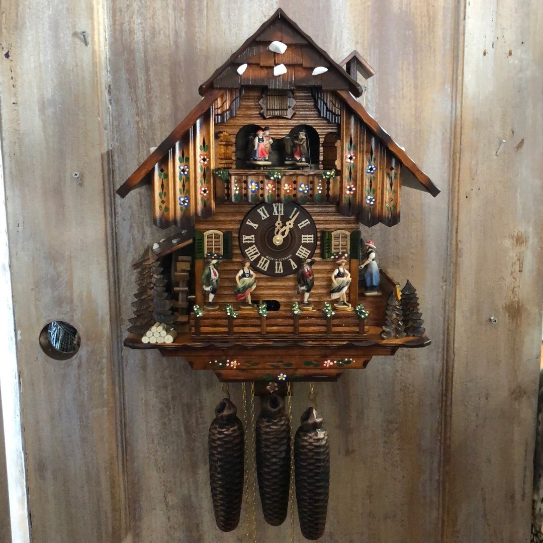 Painted chalet clock hanging on a weathered wooden door, with dancing figures, water wheel and three pinecone weights 12