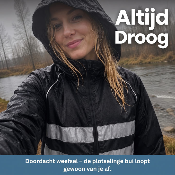 Smiling woman in a hooded dark jacket with reflective stripes and rain droplets, standing by a river on a gray day.