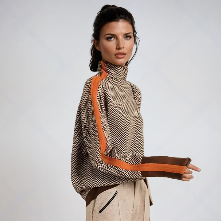 Model in profile wears the brown and cream herringbone high-neck sweater with an orange stripe down the sleeve, brown cuffs and beige trousers. 1