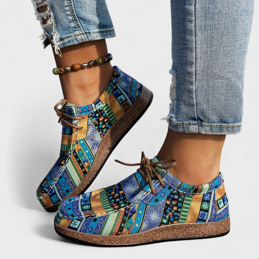 Lace-up sneakers in a blue, teal, green and gold patterned fabric with brown cork-style soles.