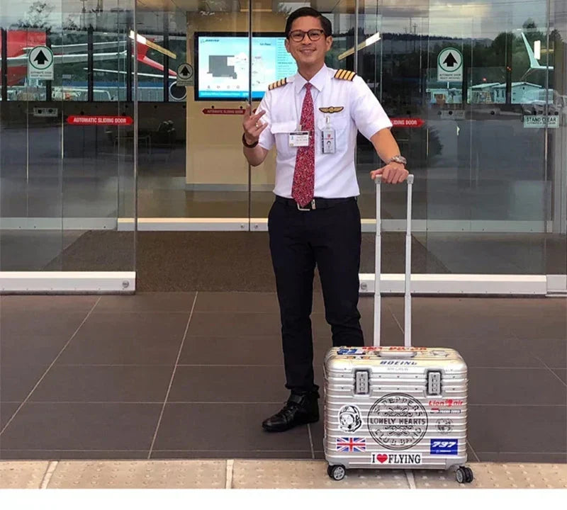 Smiling airline pilot in uniform holds the handle of a silver case covered in travel stickers 4