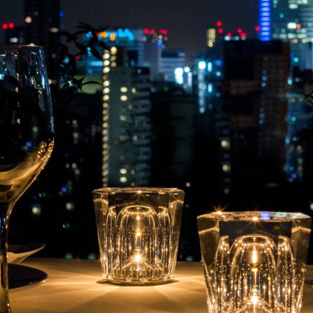 Gold transparent crystal table lamp, another view, glowing beside a wine glass on a table.